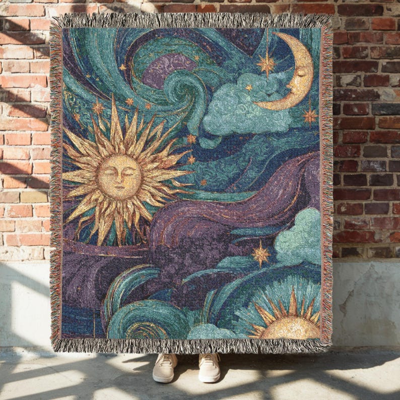 May include: Woven throw blanket featuring a celestial design with a sun, moon, stars, and clouds in shades of gold, teal, purple, and blue. The blanket has a fringed edge and is displayed against a brick wall.