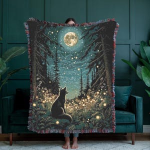 May include: Woven throw blanket featuring a forest scene with a full moon, a black fox silhouette, and twinkling lights. The blanket has a dark blue and green color palette with fringed edges. The design evokes a sense of wonder and nature.