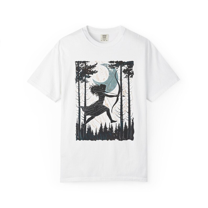 May include: White t-shirt featuring a black and teal graphic of a person with a bow and arrow, running through a forest under a crescent moon. The design includes silhouettes of trees and a forest floor.
