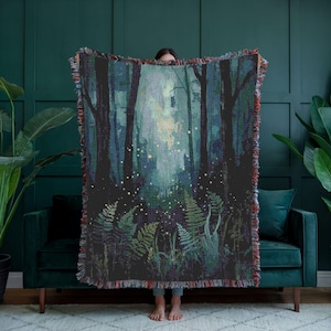 Puede incluir: Una manta tejida que representa una escena de bosque con árboles altos y helechos. La obra de arte representa un bosque místico con una fuente de luz en el centro, creando un brillo suave. La manta tiene un borde con flecos.