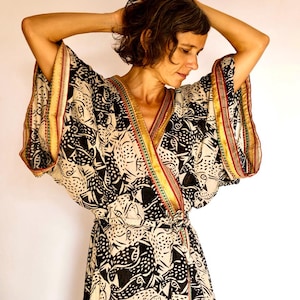 Puede incluir: Un vestido de envoltura con estampado en blanco y negro con ribetes dorados, rojos y verdes. El vestido tiene cuello en V y mangas largas.