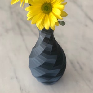 May include: A dark gray geometric vase with a twisted design holds a bouquet of yellow daisies.