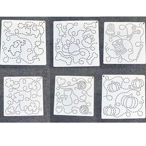 Può includere: Sei stencil bianchi per quilting con vari disegni, tra cui cuori, impronte di zampe, ossa, rocchetti di filo, zucche e gomitoli di lana. Ogni stencil ha una forma quadrata con un motivo a linea tratteggiata. Gli stencil sono disposti su una superficie grigia.