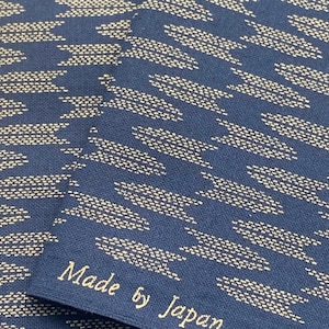 Op de afbeelding: Twee stukken donkerblauwe stof met een wit geometrisch patroon. De stof heeft de tekst "Made by Japan" erop gedrukt.
