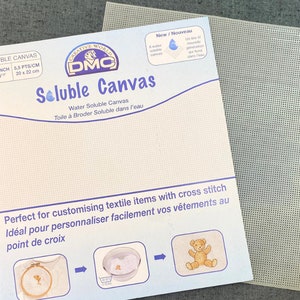 May include: DMC Soluble Canvas package, 20 x 22 cm, with a separate sheet of perforated canvas. The package features English and French text, a logo, and illustrations. The canvas is designed for cross-stitch projects and is water-soluble.