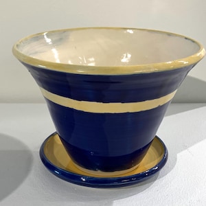 May include: A blue ceramic planter with a yellow rim and two yellow bands around the middle. The planter has a matching saucer.