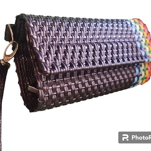 May include: Black woven clutch with a wrist strap and silver-tone hardware. The clutch features a rainbow-colored accent on the edge. The woven design gives the clutch a textured appearance. The wrist strap is made of a dark, textured material.