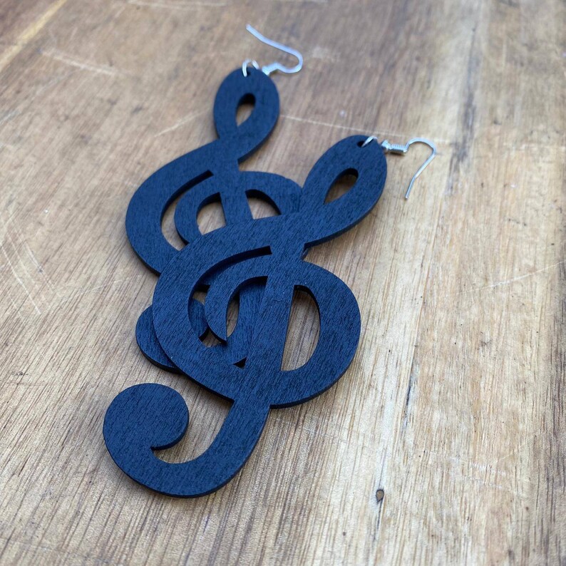 May include: A pair of black wooden earrings shaped like treble clefs. The earrings are dangling and have silver hooks.