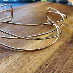 May include: A gold-toned metal choker necklace with a simple, geometric design. The necklace is made of multiple thin, interwoven bands.