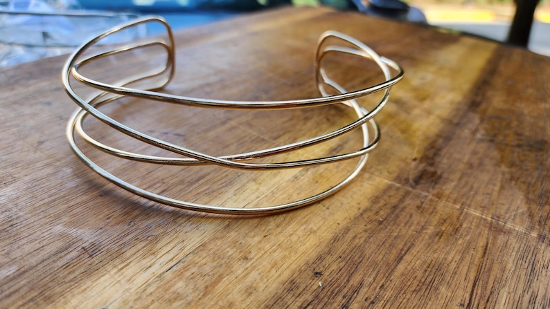 May include: A gold-toned metal choker necklace with a simple, geometric design. The necklace is made of multiple thin, interwoven bands.