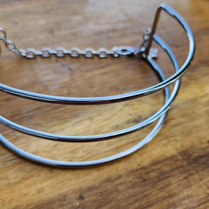 May include: A silver metal choker necklace with a double-layered design and a chain closure.