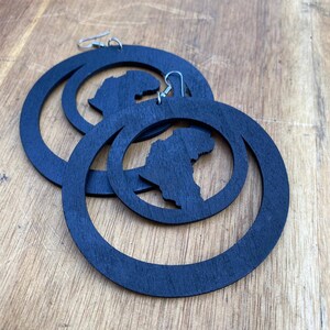 May include: A pair of black wooden hoop earrings with a cutout of the continent of Africa. The earrings are large and have a simple, modern design.