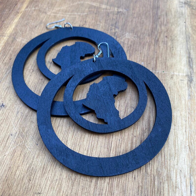 May include: A pair of black wooden hoop earrings with a cutout of the continent of Africa. The earrings are large and have a simple, modern design.