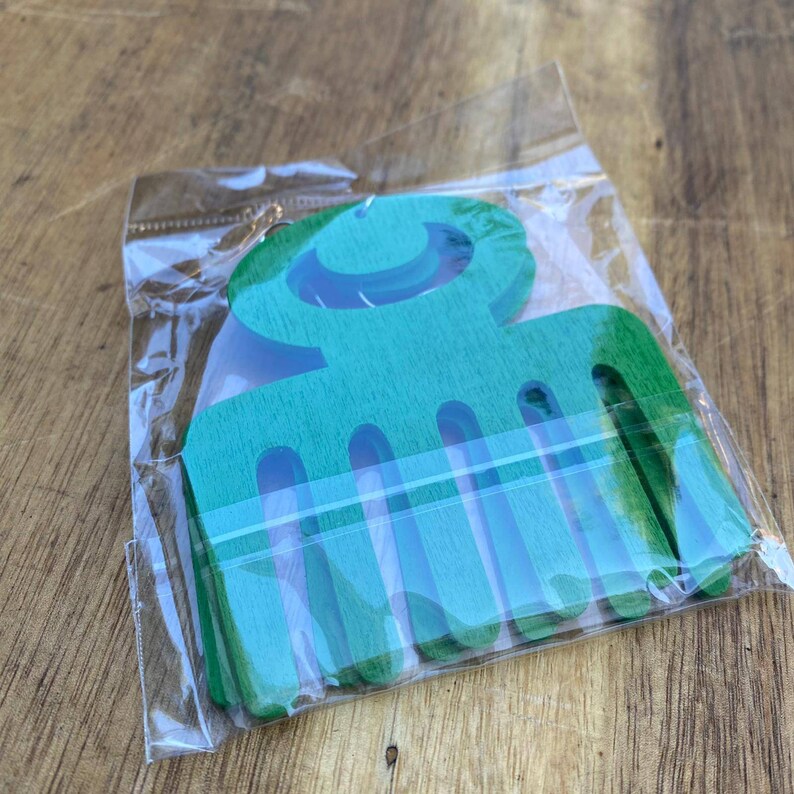May include: A green wooden comb with a crescent moon design. The comb is packaged in a clear plastic bag.