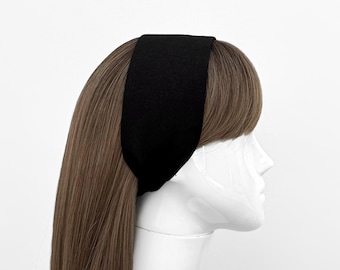Puede incluir: Una diadema negra se muestra en una cabeza de maniquí con cabello castaño. La diadema es ancha y cubre la frente. El fondo es blanco liso.