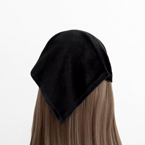 May include: A solid black velvet bandana worn over long, straight, light brown hair. The fabric has a soft, matte texture and is folded into a triangular shape that covers the top and back of the head, draping down to a point at the nape.
