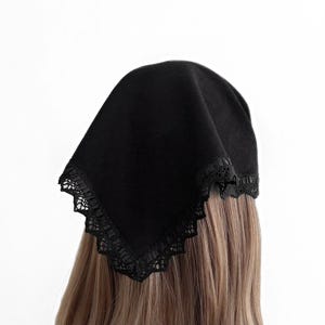 May include: A black head covering with a square shape and a delicate lace trim along the edges. The head covering is made of a soft, dark fabric and is worn on the head.