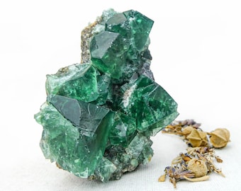 Könnte beinhalten: Ein Cluster aus grünen Fluoritkristallen mit einer rauen, natürlichen Textur. Die Kristalle sind in Pyramidenform angeordnet und haben ein durchscheinendes, glasartiges Aussehen.