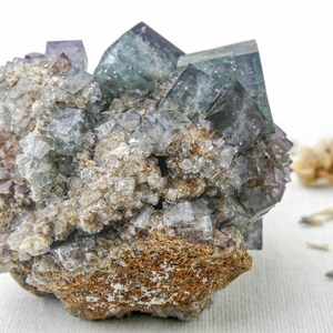 K&ouml;nnte beinhalten: Ein Cluster aus gr&uuml;nen und violetten Fluoritkristallen, eingebettet in eine braune Gesteinsmatrix. Die Kristalle sind scharf und gut definiert, mit einem glasartigen Glanz.