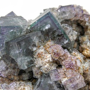 K&ouml;nnte beinhalten: Ein Cluster aus gr&uuml;nen und violetten Fluoritkristallen mit einer rauen, nat&uuml;rlichen Textur. Die Kristalle sind w&uuml;rfelf&ouml;rmig und haben einen glasartigen Glanz.