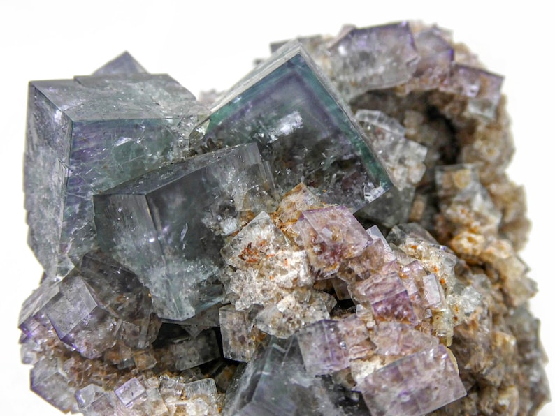 K&ouml;nnte beinhalten: Ein Cluster aus gr&uuml;nen und violetten Fluoritkristallen mit einer rauen, nat&uuml;rlichen Textur. Die Kristalle sind w&uuml;rfelf&ouml;rmig und haben einen glasartigen Glanz.