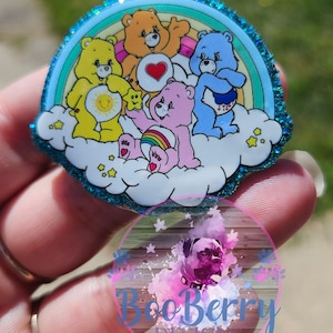 May include: A colourful Care Bears design with a rainbow and stars on a blue glitter background. The Care Bears are sitting on a cloud and are smiling.