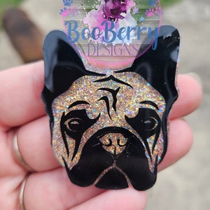 May include: A black and gold glitter French bulldog face cutout. The cutout is made of clear acrylic and has a glossy finish.