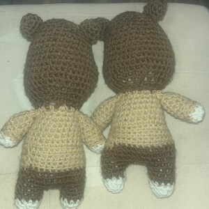 May include: Two handmade crochet bear dolls. The bears have brown heads with small ears, tan bodies, and brown legs. The feet and the tips of the arms are white. The bears are holding hands.