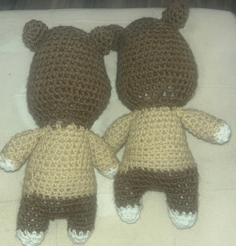 May include: Two handmade crochet bear dolls. The bears have brown heads with small ears, tan bodies, and brown legs. The feet and the tips of the arms are white. The bears are holding hands.