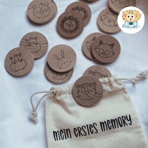 May include: A set of wooden memory game tiles featuring various animal illustrations, including a tiger, rabbit, hippopotamus, lion, raccoon, and panda. The tiles are in a white drawstring bag with the text "mein erstes memory" printed on it.