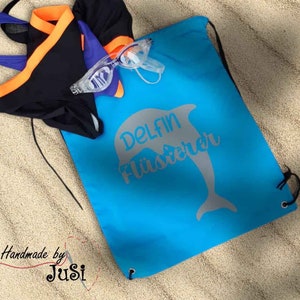 Op de afbeelding: Een blauwe trekkoordtas met een witte dolfijn afbeelding en de tekst "Delfin Flüsterrer".