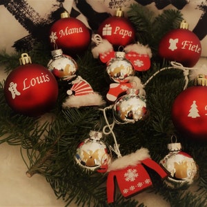 Könnte beinhalten: Rote und silberne Weihnachtskugeln mit darauf geschriebenen Namen, darunter "Mama", "Papa", "Fiete", "Louis" und "Felix".