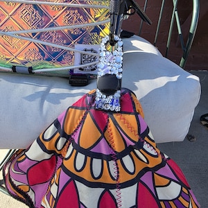 May include: A black rectangular accessory adorned with clear, white, and blue star and flower-shaped rhinestones, featuring a central black circular component. It is attached to a vibrant fabric item with a geometric pattern in orange, pink, and black.