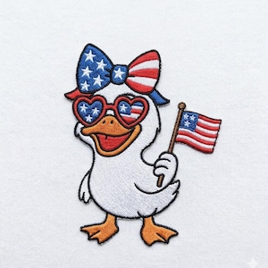 Könnte beinhalten: Ein gestickter Aufnäher mit einer weißen Ente mit orangefarbenem Schnabel und Füßen. Die Ente trägt eine Schleife und eine herzförmige Sonnenbrille, beide mit rot-weiß-blauen Sternen und Streifen gemustert. Sie hält eine kleine US-Flagge.