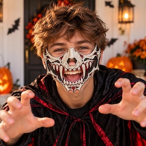 Könnte beinhalten: Eine Gesichtsmaske mit einem detaillierten silber-schwarzen Totenkopf-Design mit scharfen, markanten Zähnen und roten Akzenten. Die Maske bedeckt den Nasen- und Mundbereich und zeigt ein strukturiertes, geschichtetes Aussehen mit Details.
