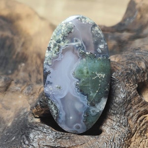 May include: A green, white, and gray agate cabochon with a swirling pattern. The cabochon is oval shaped and has a smooth, polished surface.
