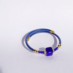 May include: A blue leather wrap bracelet with a large, square, dark blue glass bead and gold accents.