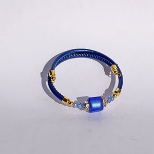May include: A blue leather bracelet with a gold clasp and a blue glass bead with rhinestones.