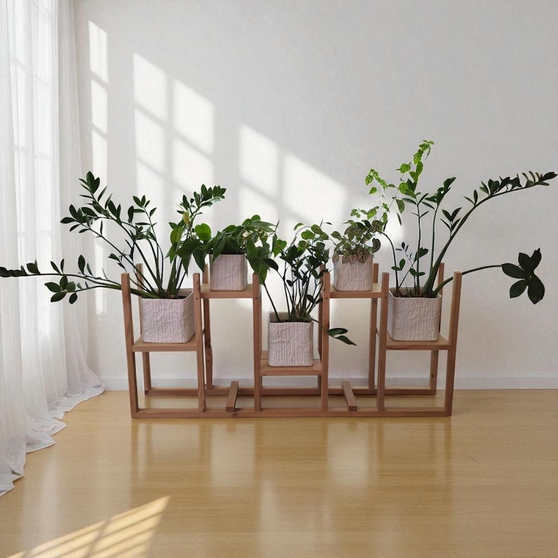 May include: A wooden plant stand with five sections, each holding a square, textured pot filled with greenery. The stand is made of light-colored wood and is placed against a white wall with natural light.