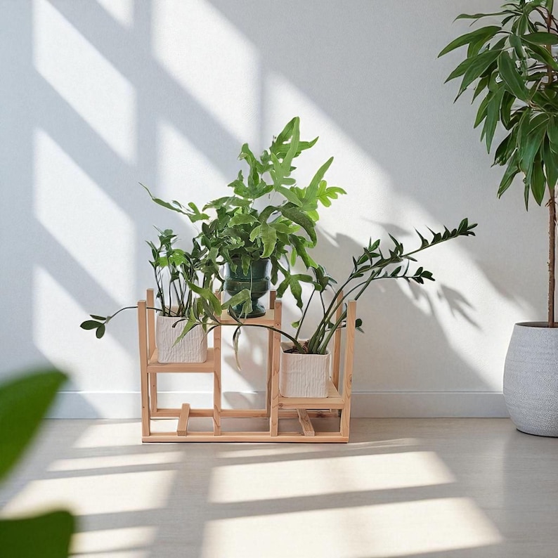 May include: A wooden plant stand with three levels, holding various potted green plants. The stand has a geometric design and is made of light-colored wood. The plants are in white and green pots, creating a natural, indoor aesthetic.