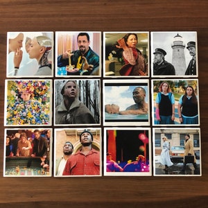 May include: A set of 12 square coasters featuring images from popular movies. The coasters are white with a black border and feature a variety of scenes and characters from different films.