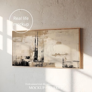 以下が含まれることがあります： ベージュの背景に黒とグレーの筆致が施された、額縁に入った抽象画。絵は白い壁にかけられている。