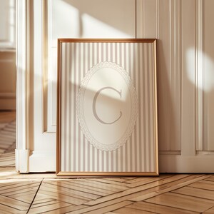 Heirloom-inspired monogram nursery wall art featuring the initial 'C' within a lace frame against classic pink and white stripes.  A natural fit for interiors inspired by the feminine, refined aesthetic of spaces thoughtfully curated by Anthropologie and Studio McGee.