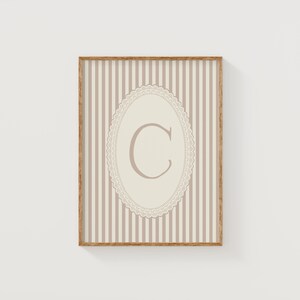 Heirloom-inspired monogram nursery wall art featuring the initial 'C' within a lace frame against classic pink and white stripes.  A natural fit for interiors inspired by the feminine, refined aesthetic of spaces thoughtfully curated by Anthropologie and Studio McGee.