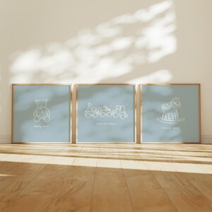 May include: Three framed prints with a light blue background and gold frames. Each print features a white line drawing of a toy: a teddy bear, a train, and a rocking horse. The text "teddy bear", "choo choo train", and "rocking horse" are below each image.