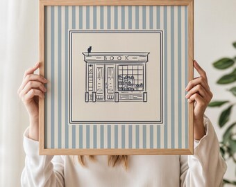 May include: A framed print featuring a bookstore illustration. The artwork is in black and white, with the word "BOOK" above the store's entrance. The frame has a light wood finish, and the background has blue and white vertical stripes.