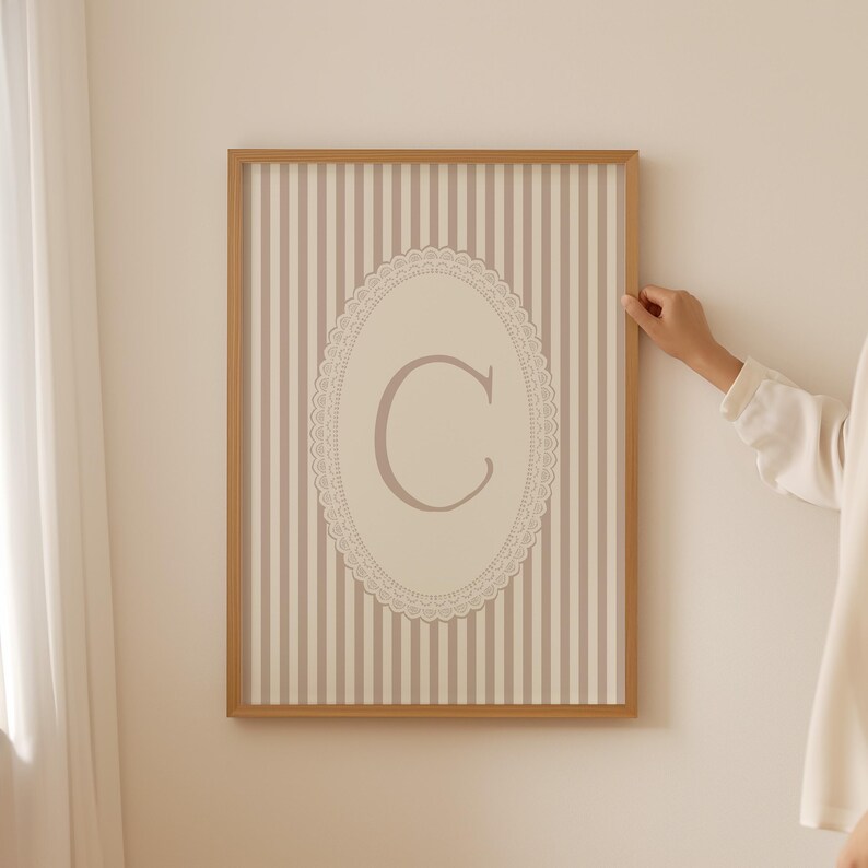 Heirloom-inspired monogram nursery wall art featuring the initial 'C' within a lace frame against classic pink and white stripes.  A natural fit for interiors inspired by the feminine, refined aesthetic of spaces thoughtfully curated by Anthropologie and Studio McGee.