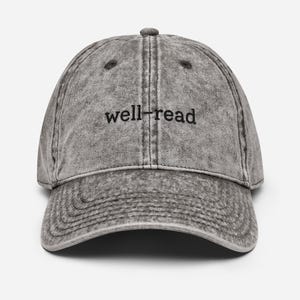 May include: A grey, vintage-style baseball cap with the text "well-read" in black. The cap has a curved peak and a distressed appearance, suggesting a worn or retro aesthetic. The hat is a classic six-panel design.