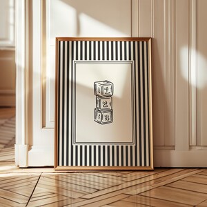 Peut inclure: Une impression encadrée avec une bordure dorée, représentant une illustration en noir et blanc de trois blocs de jouets empilés, numérotés de un à trois. Le cadre présente un motif à rayures noires et blanches.