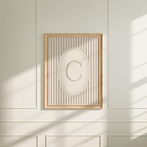 Heirloom-inspired monogram nursery wall art featuring the initial 'C' within a lace frame against classic pink and white stripes.  A natural fit for interiors inspired by the feminine, refined aesthetic of spaces thoughtfully curated by Anthropologie and Studio McGee.